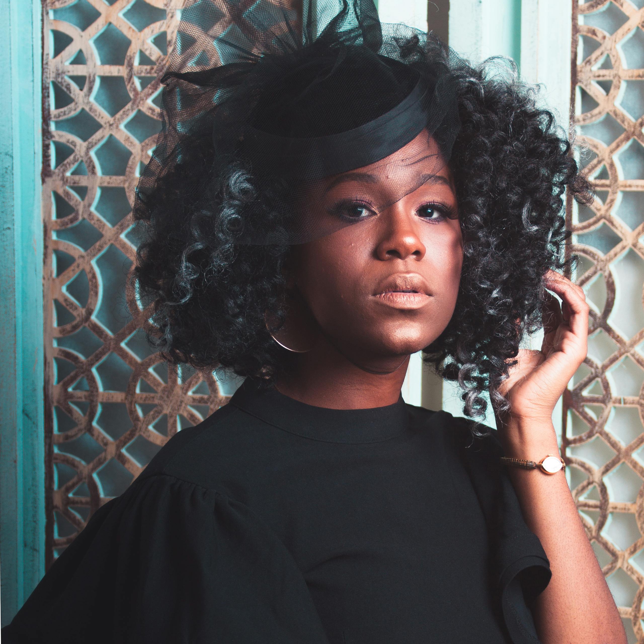 Stylish woman posing in elegant attire with curly hair and a decorative hat.